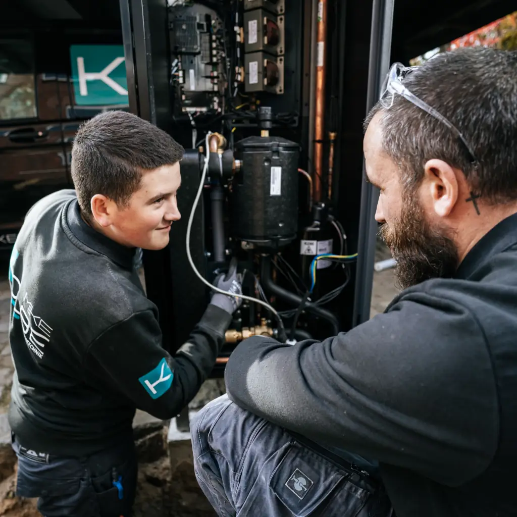 Zwei Mitarbeiter von Mike Kolbe Heizungstechnik bei der Arbeit an einer Heizungsanlage. Der junge Heizungstechniker wird vom erfahrenen Anlagenbauer unterstützt.